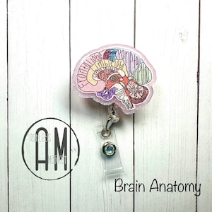 May include: A pink glitter brain anatomy badge reel with a clear plastic badge holder and a sparkly iridescent button. The brain is labeled with the different lobes and structures. The text "Brain Anatomy" is printed below the badge reel.