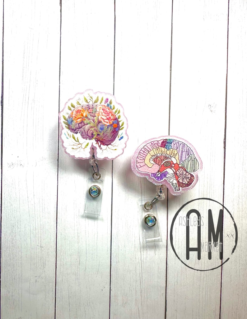 May include: Two pink and white brain-shaped badge reels with a floral design and a diagram of the brain. The badge reels have clear plastic clips and iridescent blue retractable badge holders.