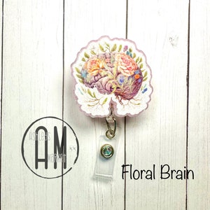 May include: A pink and white floral brain design on a clear plastic badge reel with a gold chain and a clear plastic badge holder. The text "Floral Brain" is printed below the badge reel.