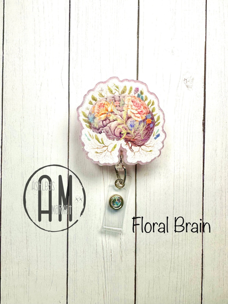 May include: A pink and white floral brain design on a clear plastic badge reel with a gold chain and a clear plastic badge holder. The text "Floral Brain" is printed below the badge reel.