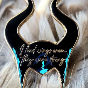 Puede incluir: Un pin de esmalte negro y dorado con forma de cuernos, con el texto "I had wings once... They were wrong." El pin tiene detalles turquesa y un dise&ntilde;o de silueta.