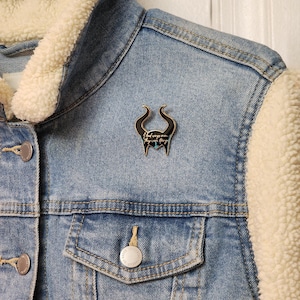 Puede incluir: Chaqueta vaquera azul claro con forro crema y difuso en el cuello y las mangas. Un pin negro y plateado en forma de cuernos est&aacute; adherido a la chaqueta. El pin tiene el texto "I had wings once, they were things."