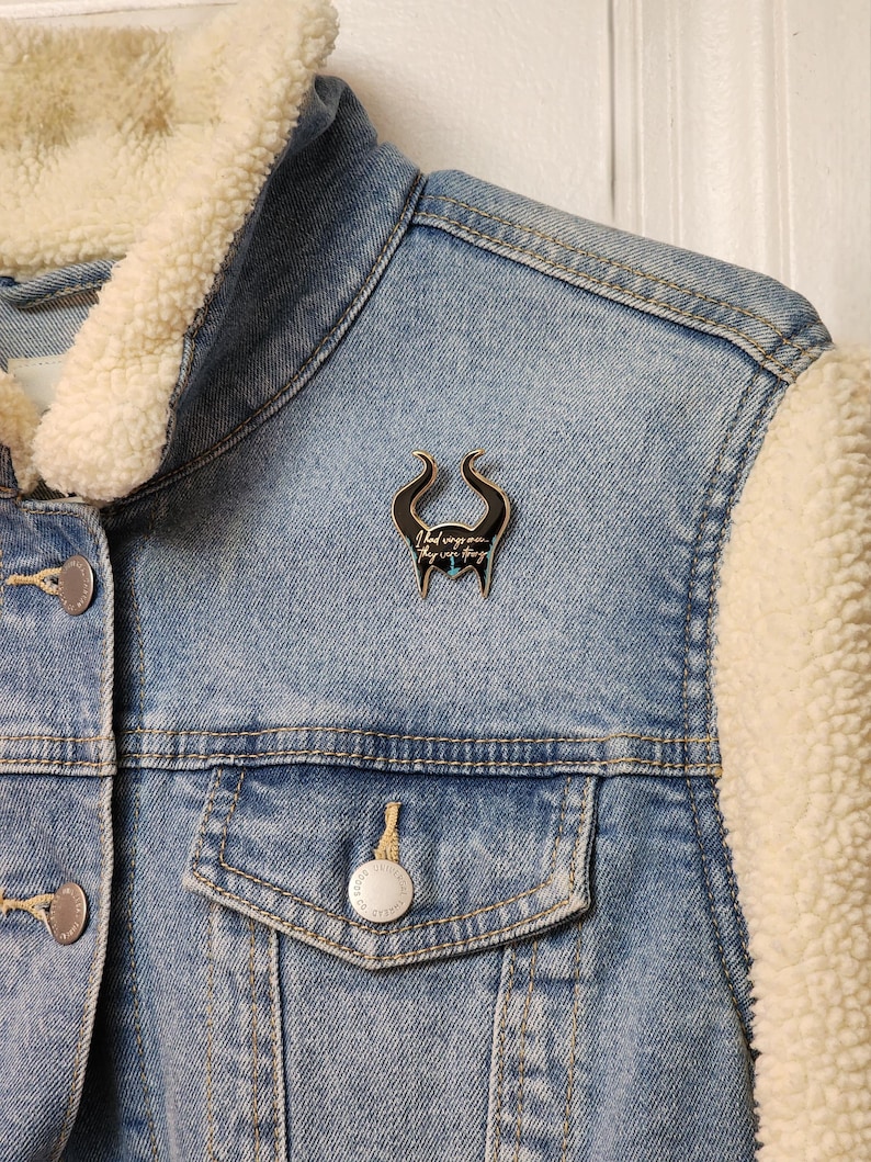Puede incluir: Chaqueta vaquera azul claro con forro crema y difuso en el cuello y las mangas. Un pin negro y plateado en forma de cuernos est&aacute; adherido a la chaqueta. El pin tiene el texto "I had wings once, they were things."