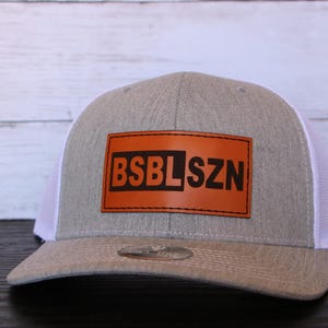 May include: A grey and white baseball cap with a brown leather patch that says "BSBLSZN".