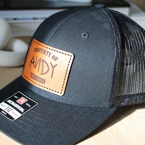 May include: Black and brown trucker hat with a leather patch that says "Property of Andy Est. 1995".