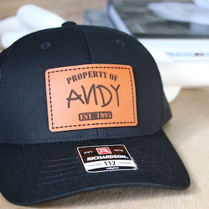 May include: Black trucker hat with a brown leather patch that says "PROPERTY OF ANDY EST. 1995".