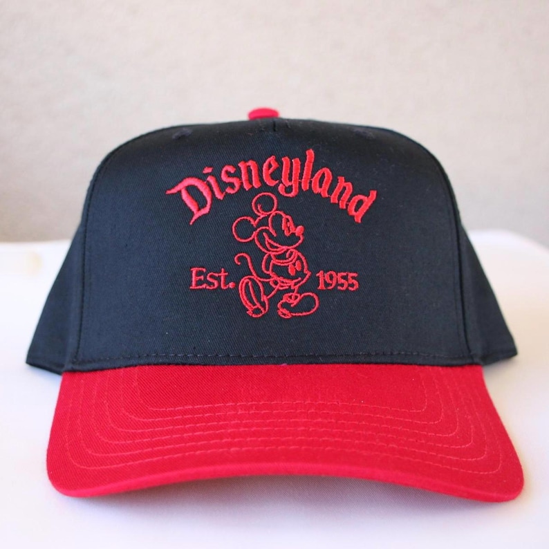 K&ouml;nnte beinhalten: Schwarze und rote Baseballkappe mit einem roten gestickten Mickey Mouse und dem Text "Disneyland Est. 1955".