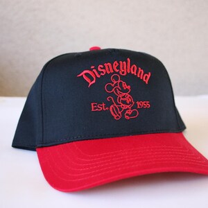 K&ouml;nnte beinhalten: Schwarze und rote Baseballkappe mit einem roten gestickten Mickey Mouse und dem Text "Disneyland Est. 1955".