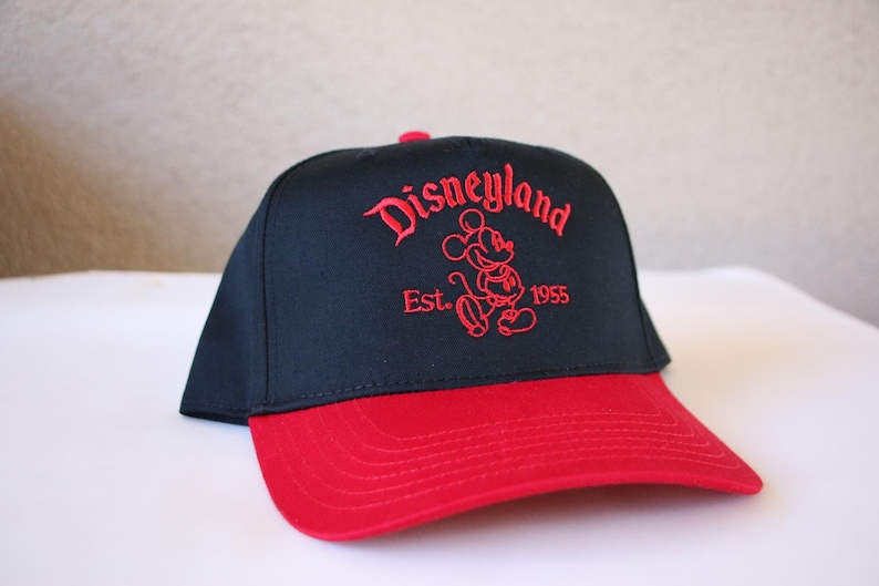 K&ouml;nnte beinhalten: Schwarze und rote Baseballkappe mit einem roten gestickten Mickey Mouse und dem Text "Disneyland Est. 1955".