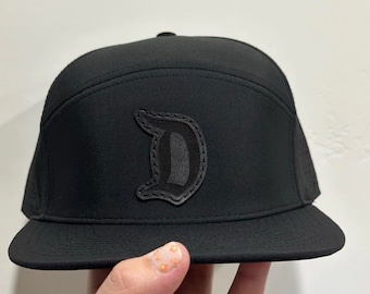 May include: A black baseball cap with a black felt letter "D" on the front.