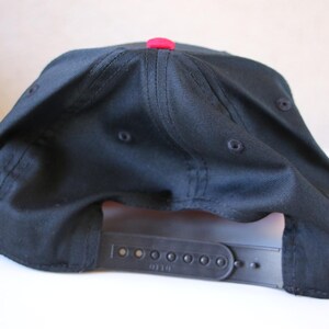 K&ouml;nnte beinhalten: Schwarze Baseballkappe mit rotem Schirm und einem schwarzen verstellbaren Riemen mit dem aufgedruckten Wort "Diesel".