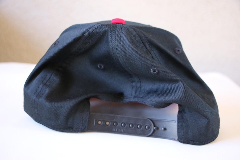 K&ouml;nnte beinhalten: Schwarze Baseballkappe mit rotem Schirm und einem schwarzen verstellbaren Riemen mit dem aufgedruckten Wort "Diesel".