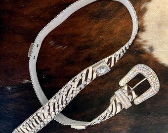 May include: A white and black zebra print belt with clear rhinestones and a large, clear rhinestone buckle.