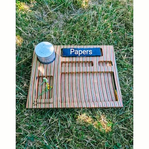 Könnte beinhalten: Ein Holz-Rolltablett mit einem gestreiften Design. Es hat ein kleines Fach für einen Grinder, ein größeres Fach für Papiere und ein kleines Fach für andere Gegenstände. Das Tablett ist mit "Papers" und "HEXAGONIA" beschriftet.