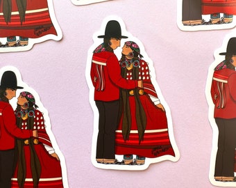 Puede incluir: Una pegatina con una pareja vestida con ropa tradicional indígena. El hombre lleva una camisa roja, pantalones negros y un sombrero negro. La mujer lleva un vestido rojo con rayas blancas y negras, un cinturón negro y una pañoleta roja. La pegatina tiene el texto "Jamie Whiteduck" en la parte inferior.