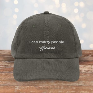 May include: A dark green corduroy baseball cap with white embroidery that reads "I can marry people officiant".