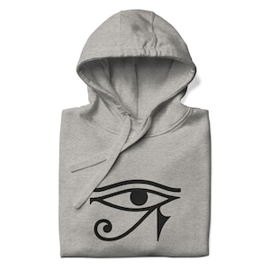 Puede incluir: Una sudadera con capucha gris con un símbolo negro del Ojo de Horus en la parte delantera.