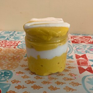 May include: A glass jar filled with layered yellow and white slime. The slime is topped with a white swirl.