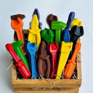 Könnte beinhalten: Eine Holzkiste gefüllt mit bunten Crayon-Werkzeugen, darunter ein Schraubenschlüssel, ein Schraubendreher, eine Zange und ein Hammer. Die Stifte sind in Form verschiedener Werkzeuge geformt.