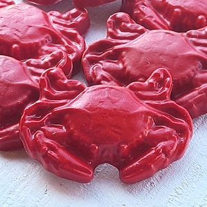 Könnte beinhalten: Mehrere hellrote, krabbenförmige Objekte sind eng beieinander angeordnet. Die Krabben haben eine glänzende Oberfläche und detaillierte Merkmale, einschließlich Scheren und segmentierter Körper. Die Objekte scheinen dekorativ oder möglicherweise essbar zu sein, mit einer lebendigen, auffälligen Farbe.
