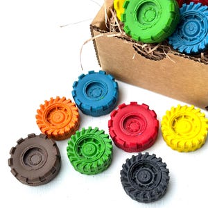 May include: A selection of brightly coloured toy tractor tyres in shades of red, yellow, green, blue, orange, brown, and black. Some tyres are in a cardboard box with shredded paper, others are on a white surface.