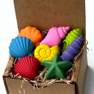 Könnte beinhalten: Ein Karton gefüllt mit bunten, muschelförmigen Wachsmalstiften. Die Wachsmalstifte sind in verschiedenen Farben erhältlich, darunter Blau, Orange, Rosa, Gelb, Grün, Rot und Lila. Die Box ist mit geschreddertem Papier gefüllt.