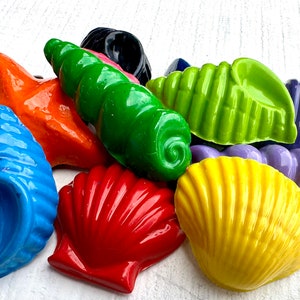 Könnte beinhalten: Eine Sammlung bunter Muscheln in verschiedenen Formen und Größen. Die Muscheln bestehen aus einem glatten, glänzenden Material und sind in leuchtenden, kräftigen Farben bemalt, darunter Blau, Grün, Gelb, Rot, Orange und Lila.