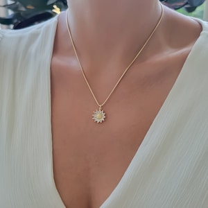 May include: A gold chain necklace with a small sunflower pendant. The sunflower is made of gold and has a white center.