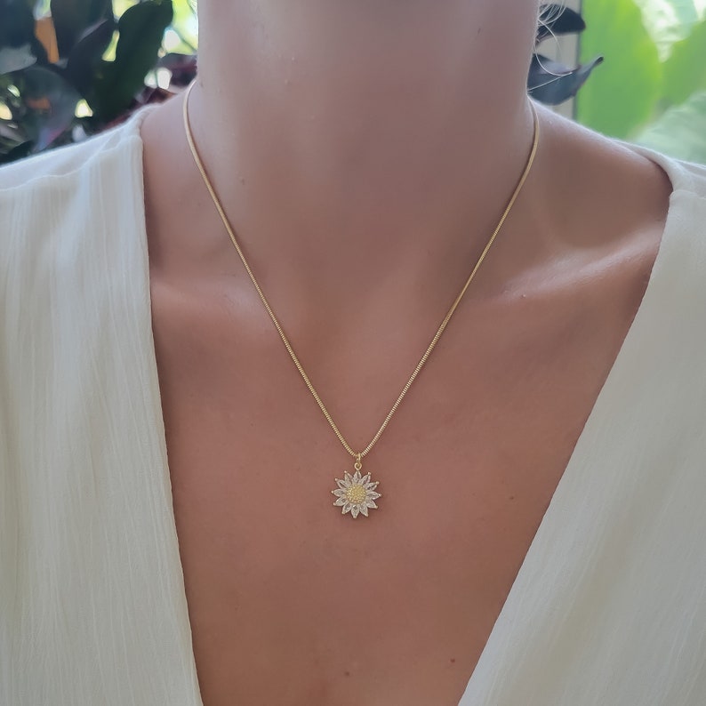 May include: A gold chain necklace with a small sunflower pendant. The sunflower is made of clear and yellow cubic zirconia stones.