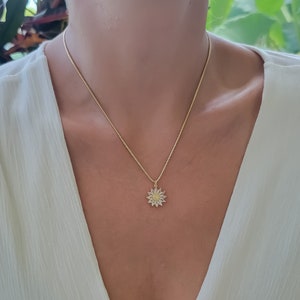 May include: A gold chain necklace with a delicate sunflower pendant. The sunflower is made of gold and has a yellow center with white petals.