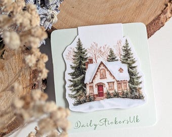 May include: A sticker featuring a winter scene with a snow-covered cottage, evergreen trees, and bare trees. The cottage has a red door and is surrounded by snow. The text "Daily Stickers Uk" is written in cursive at the bottom.