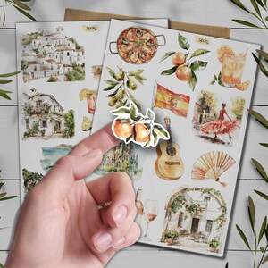May include: Watercolor stickers with Spanish themes. Illustrations include paella, oranges, a Spanish flag, a flamenco dancer, a guitar, and architectural scenes. The word "Spain" is written on the stickers.