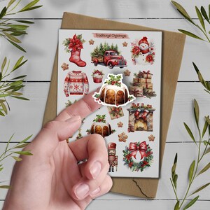 May include: A sticker sheet titled Traditional Christmas featuring watercolor illustrations of a red stocking, a red truck with trees, a snowman, a sweater, a Christmas pudding, wrapped gifts, a fireplace, a nutcracker, and a wreath.
