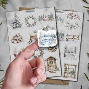 May include: Sheets of winter-themed stickers featuring watercolor illustrations of snowy landscapes, cabins, wreaths, and trees. The text "Winter Forest" is printed at the top of the sheets. The stickers are held by a person's finger.