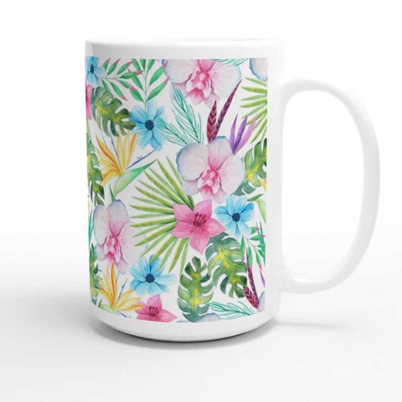 May include: White ceramic mug featuring a tropical floral pattern. The design incorporates pink, blue, yellow, and green flowers and leaves against a white backdrop.