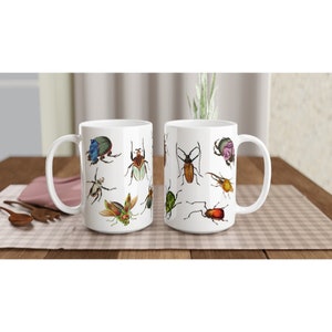 Puede incluir: Dos tazas de cer&aacute;mica blanca con un dise&ntilde;o de insectos coloridos. Las tazas presentan una variedad de escarabajos, mariposas y otros insectos en un estilo vintage.