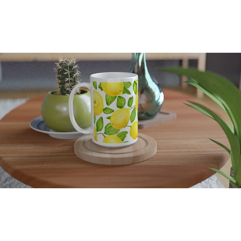 K&ouml;nnte beinhalten: Wei&szlig;e Keramiktasse mit Zitronenmuster. Die Tasse hat einen wei&szlig;en Henkel und ist mit Zitronen und gr&uuml;nen Bl&auml;ttern gef&uuml;llt.