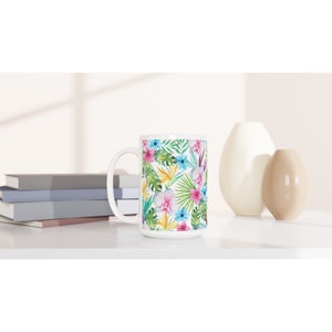 May include: White ceramic mug featuring a tropical floral design. The pattern includes pink, blue, yellow, and green flowers and leaves.