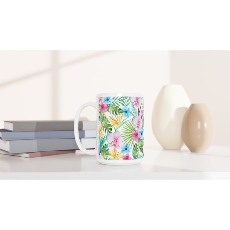 May include: White ceramic mug featuring a tropical floral design. The pattern includes pink, blue, yellow, and green flowers and leaves.