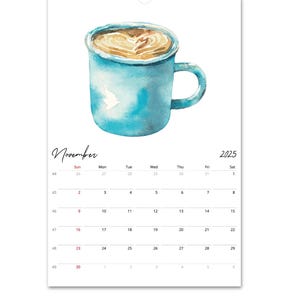 Peut inclure: Une page de calendrier mural pour novembre 2025 pr&eacute;sentant une illustration &agrave; l'aquarelle d'une tasse en c&eacute;ramique bleue remplie de caf&eacute; avec un motif de c&oelig;ur en mousse. La grille du calendrier affiche les jours du mois en noir.