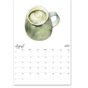 Peut inclure: Une page de calendrier mural pour ao&ucirc;t 2025 pr&eacute;sentant une illustration &agrave; l'aquarelle d'une tasse en c&eacute;ramique verte remplie d'une boisson surmont&eacute;e d'une mousse en forme de c&oelig;ur. La grille du calendrier affiche les jours avec les en-t&ecirc;tes.