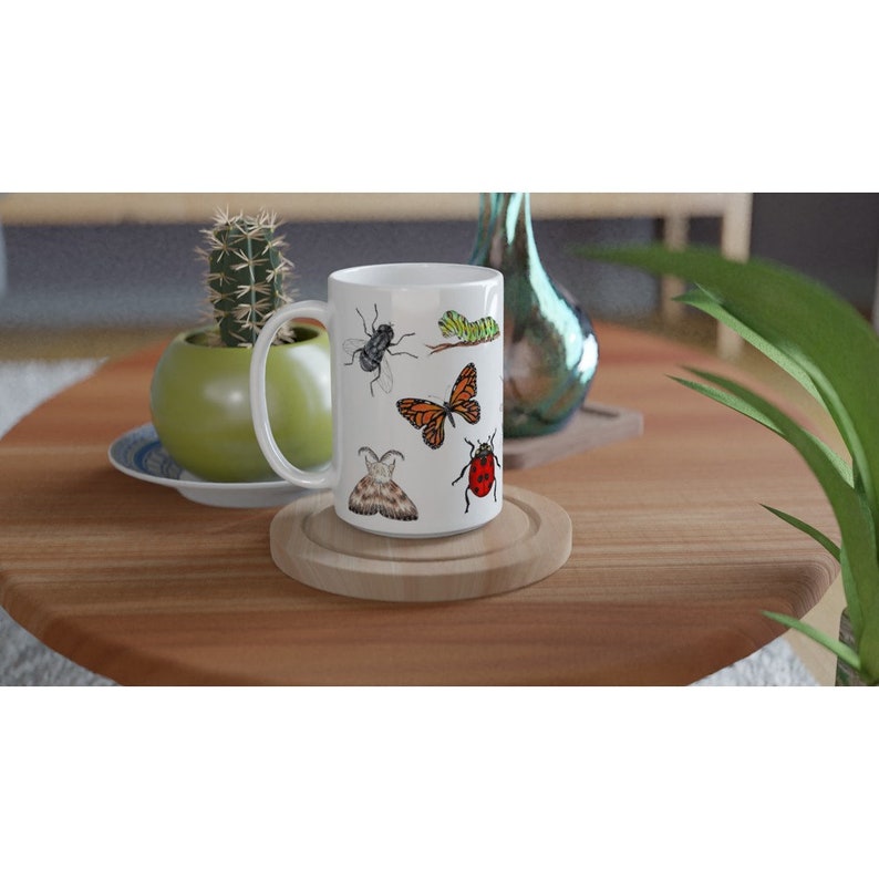 K&ouml;nnte beinhalten: Wei&szlig;e Keramiktasse mit einem bunten Insekten-Design. Die Tasse zeigt einen Schmetterling, einen Marienk&auml;fer, eine Fliege, eine Raupe und eine Motte.