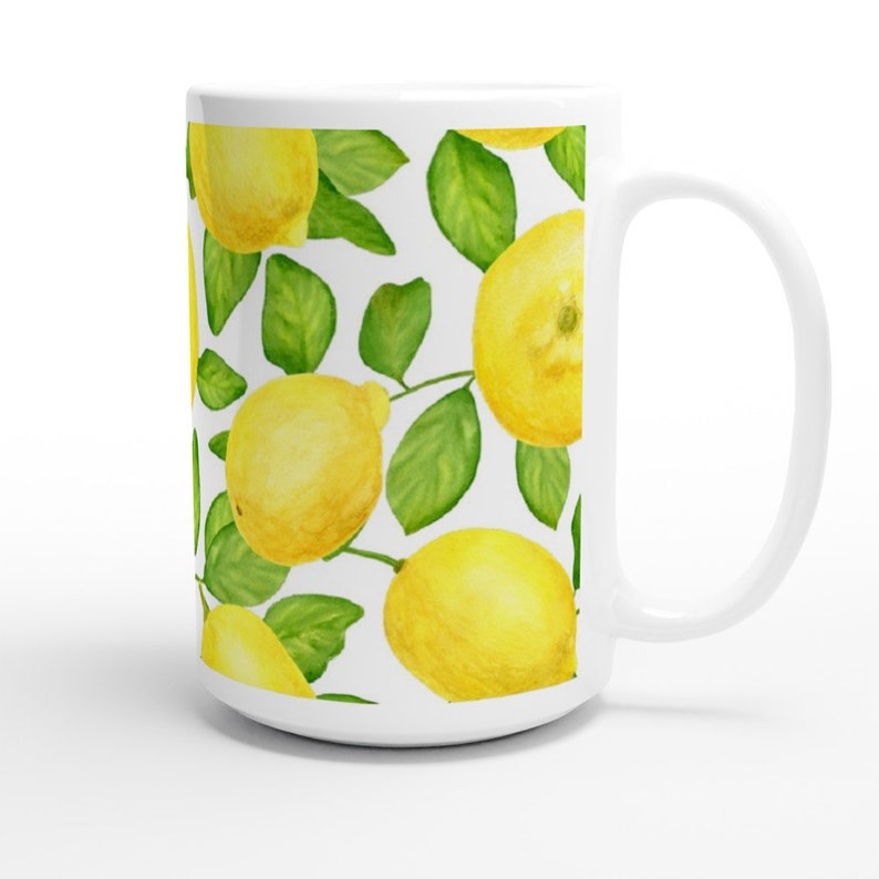 K&ouml;nnte beinhalten: Wei&szlig;e Keramiktasse mit einem Muster aus gelben Zitronen und gr&uuml;nen Bl&auml;ttern. Die Tasse hat einen wei&szlig;en Henkel.