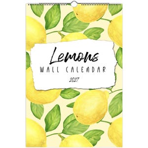 May include: A 2027 wall calendar featuring a repeating watercolor pattern of yellow lemons and green leaves on a pale yellow background. A white, torn-edge rectangular label in the center displays the text Lemons WALL CALENDAR 2027.
