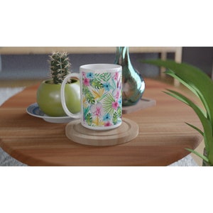 May include: White ceramic mug with a tropical floral pattern featuring pink, blue, yellow, and green flowers and leaves.
