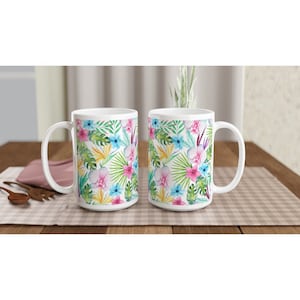 May include: Two white ceramic mugs with a tropical floral pattern. The mugs feature pink, blue, yellow, and green flowers and leaves on a white background.