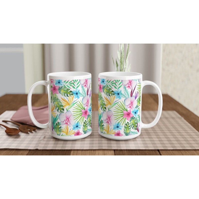 May include: Two white ceramic mugs with a tropical floral pattern. The mugs feature pink, blue, yellow, and green flowers and leaves on a white background.