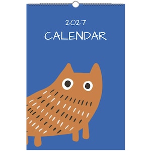 Puede incluir: Un calendario de pared 2027 con fondo azul y una ilustración de un gato marrón. El gato tiene grandes ojos blancos con pupilas negras y marcas en forma de rayas de color marrón oscuro en el cuerpo. El texto 2027 CALENDAR está en blanco.