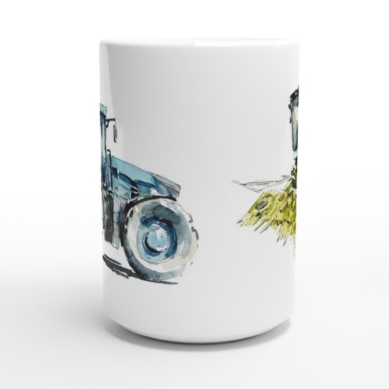 K&ouml;nnte beinhalten: Wei&szlig;e Keramiktasse mit einer Aquarell-Illustration eines blauen Traktors und einem Heuhaufen. Der Traktor befindet sich auf der linken Seite der Tasse und der Heuhaufen auf der rechten Seite.