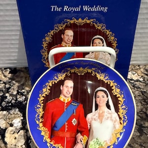 Puede incluir: Un juego de plato y caja conmemorativos de una boda real. El plato tiene un borde azul con filigrana dorada y la imagen de la pareja. La caja es azul y muestra el texto "The Royal Wedding".
